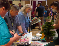 Conference attendees browse exhibitor booths, chatting with vendors and exploring educational displays in a busy exhibit hall.