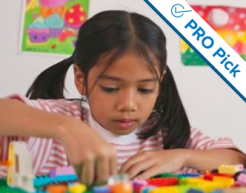 A young student plays with a table of LEGO bricks. Colorful drawings hang on the wall behind her. In the upper right corner of the image is the PRO Picks logo.