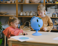 Two children interact with a globe on the table in front of them in an art classroom environment.