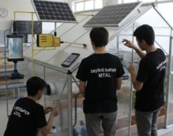 Three students work on a solar panel device in a bright white laboratory space.