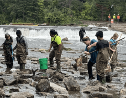 Students and teachers sift through a rocky riverbed with nets and buckets.