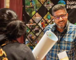 A smiling exhibitor at the NAAEE Conference hands an attendee a rolled up poster.