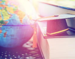 Black graduation cap on two big text books and a laptop