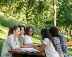Image of multiethnic group of young students sitting and studying outdoors while talking.