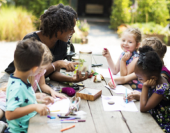 Teacher and young students sit outside with art materials
