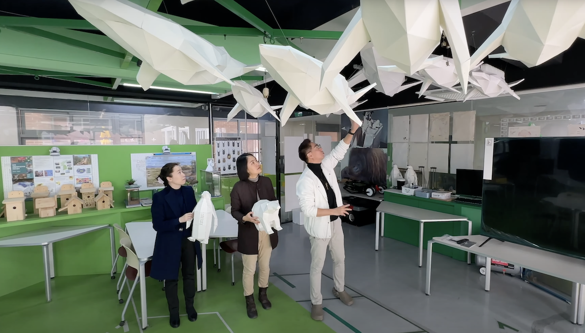 Three people look up at paper whales hanging from ceiling