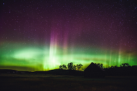 Green and purple aurora borealis fill an open night sky