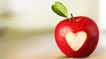 A bright red apple with a small green leaf has a piece missing in the shape of a heart. 