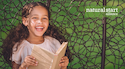 Child with long curly hair laughs while reading a book