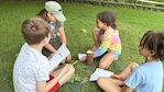 A teacher sits in the grass with students while talking about environmental education