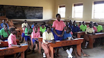 A group of uniformed students fill a classroom of long wooden desks