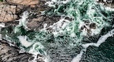 Blue-green waves crash along a rocky coast